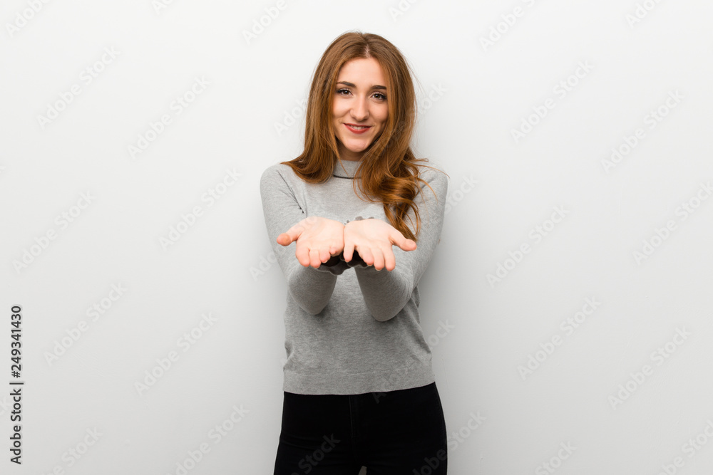 Redhead girl over white wall holding copyspace imaginary on the palm to insert an ad Redhead girl over white wall holding copyspace imaginary on the palm to insert an ad