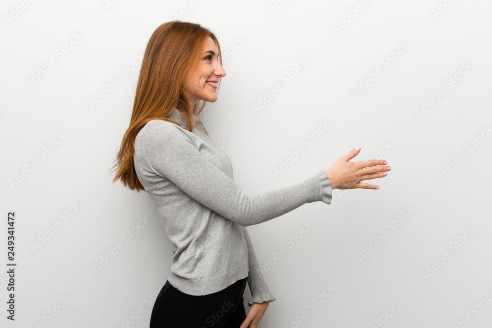 Redhead girl over white wall handshaking after good deal Redhead girl over white wall handshaking after good deal