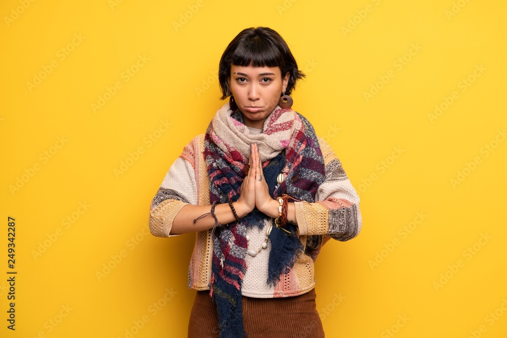 Young hippie woman over yellow wall keeps palm together. Person asks for something Young hippie woman over yellow wall keeps palm together. Person asks for something
