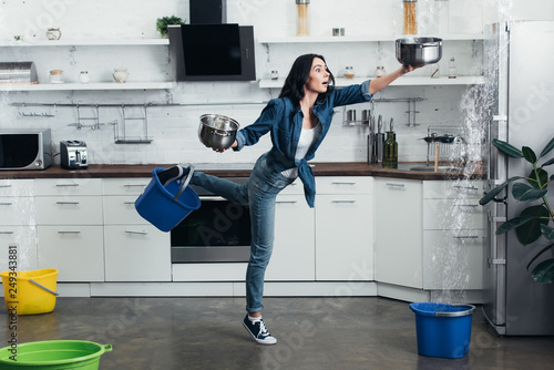 Full length view of shoked woman in jeans dealing with water leak in kitchen photo