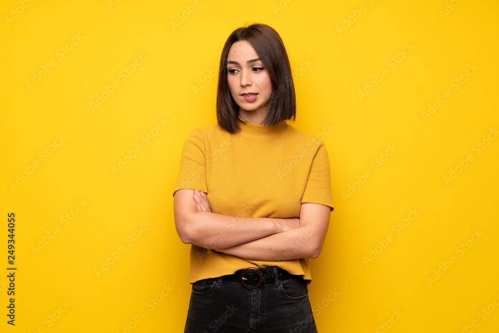 Young woman over yellow wall with confuse face expression while bites lip Young woman over yellow wall with confuse face expression while bites lip