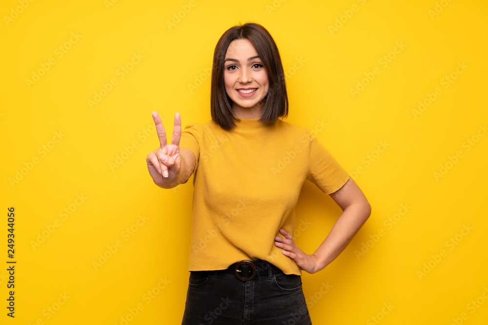 Young woman over yellow wall smiling and showing victory sign Young woman over yellow wall smiling and showing victory sign