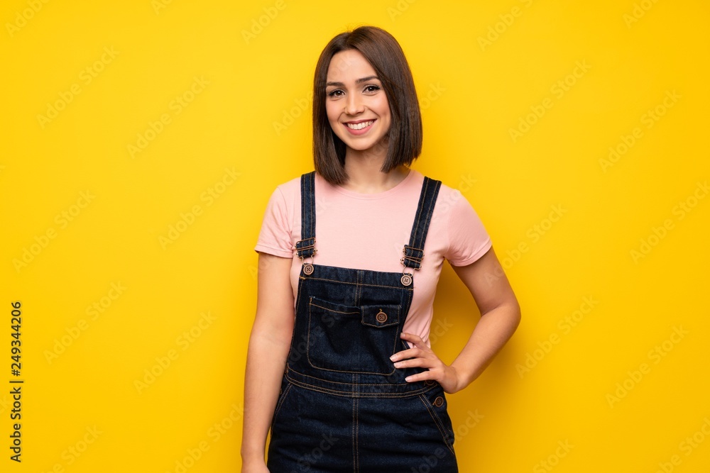 Young woman over yellow wall posing with arms at hip and smiling