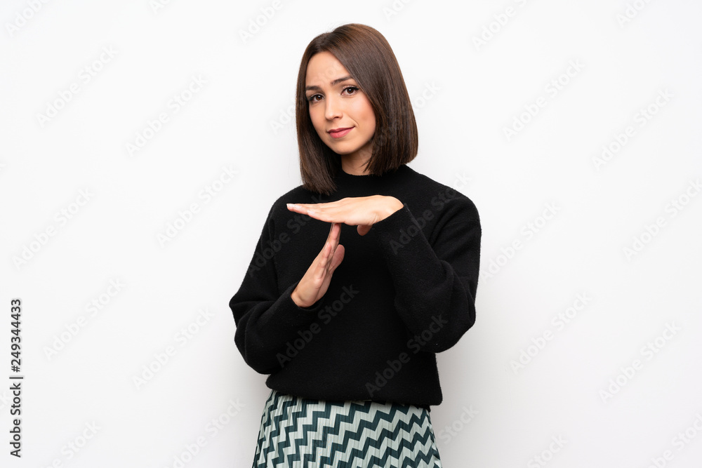 Young woman over white wall making time out gesture