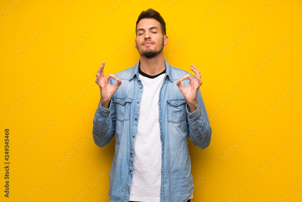 Handsome man over yellow wall in zen pose Handsome man over yellow wall in zen pose