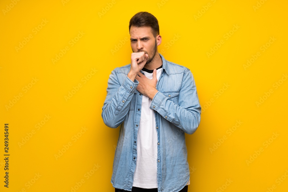 Handsome man over yellow wall is suffering with cough and feeling bad Handsome man over yellow wall is suffering with cough and feeling bad
