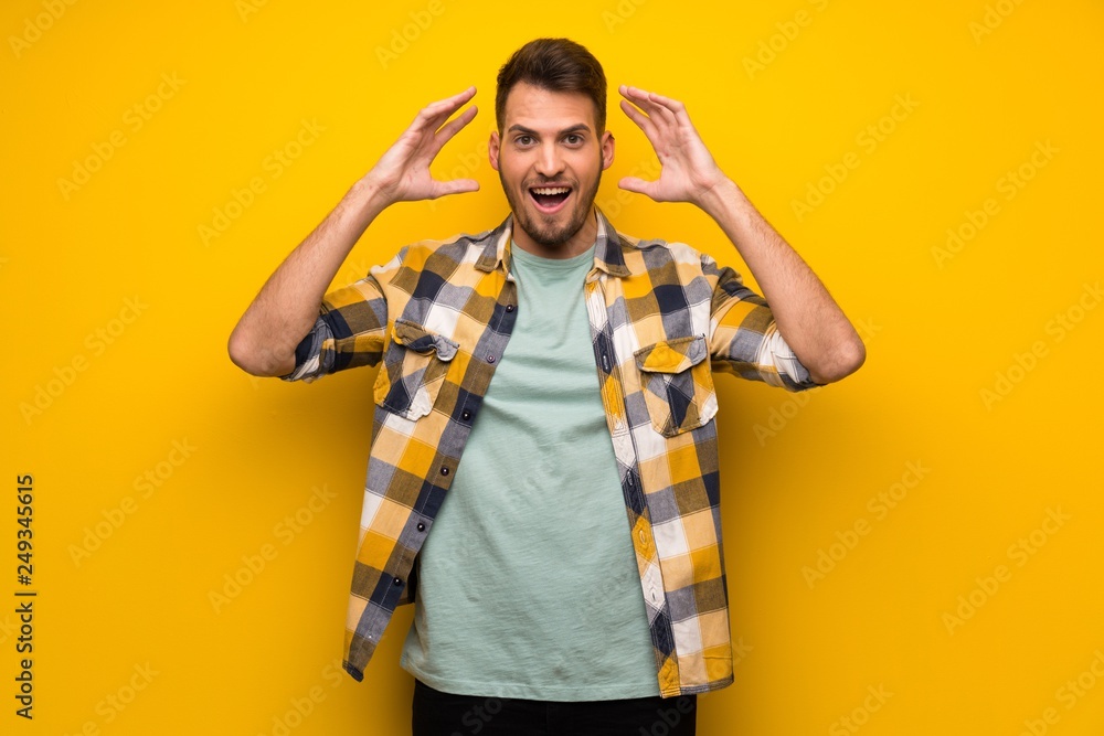 Handsome man over yellow wall with surprise and shocked facial expression Handsome man over yellow wall with surprise and shocked facial expression