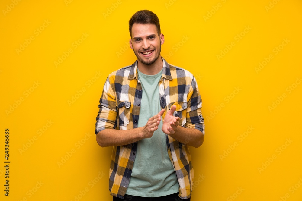 Handsome man over yellow wall applauding after presentation in a conference Handsome man over yellow wall applauding after presentation in a conference