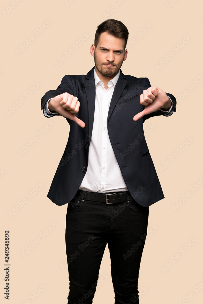 Handsome business man showing thumb dowg with negative expression over ocher background Handsome business man showing thumb dowg with negative expression over ocher background
