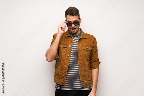 Handsome man over white wall with glasses and surprised
