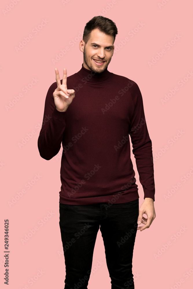 Man with turtleneck sweater smiling and showing victory sign over pink background Man with turtleneck sweater smiling and showing victory sign over pink background