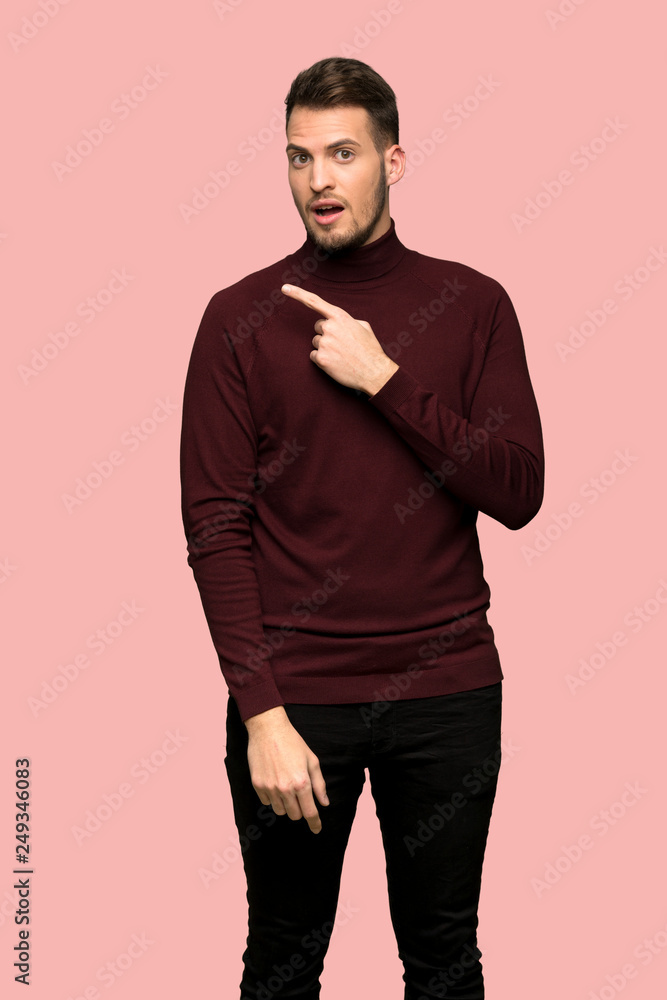 Man with turtleneck sweater surprised and pointing side over pink background Man with turtleneck sweater surprised and pointing side over pink background