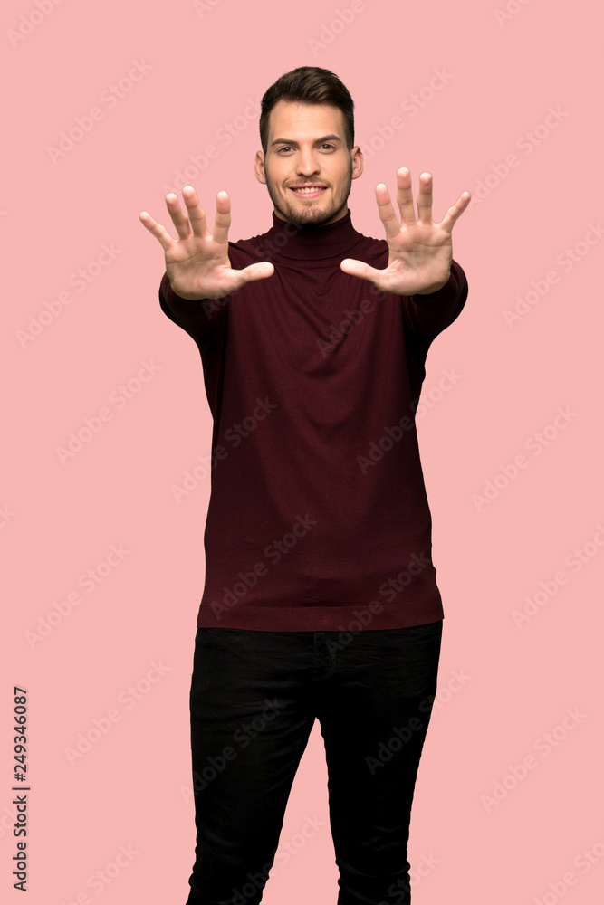 Man with turtleneck sweater counting ten with fingers over pink background Man with turtleneck sweater counting ten with fingers over pink background