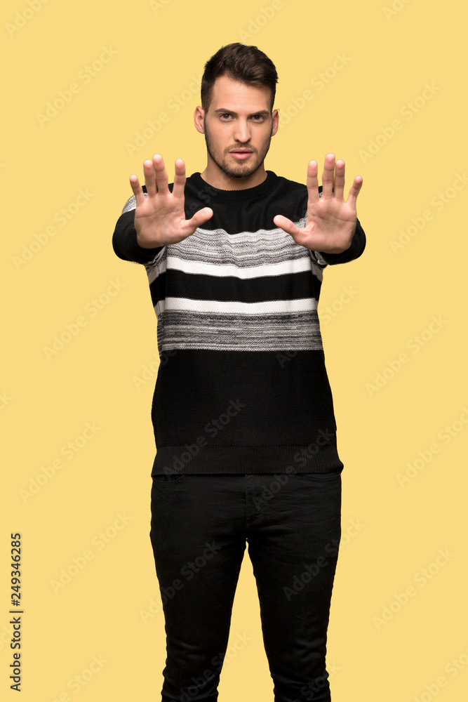 Handsome man making stop gesture and disappointed over yellow background Handsome man making stop gesture and disappointed over yellow background