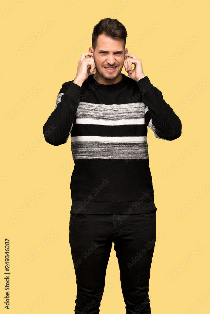 Handsome man frustrated and covering ears with hands over yellow background Handsome man frustrated and covering ears with hands over yellow background
