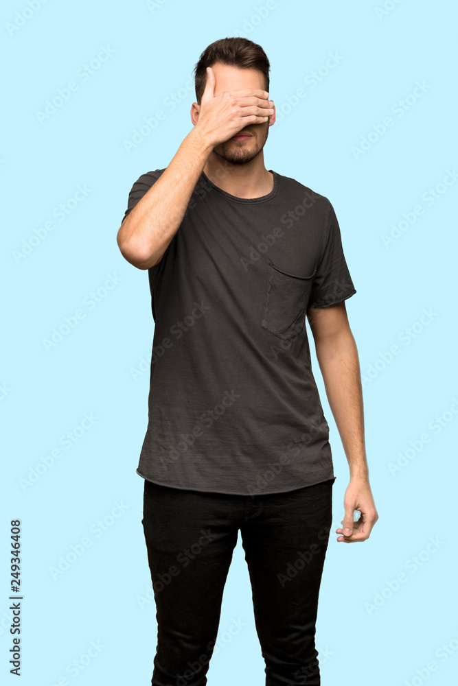 Man with black shirt covering eyes by hands. Do not want to see something over blue background Man with black shirt covering eyes by hands. Do not want to see something over blue background