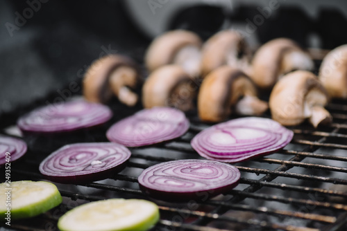 selective focus of raw onion slices, zucchini and mushrooms grilling on barbecue grill grade