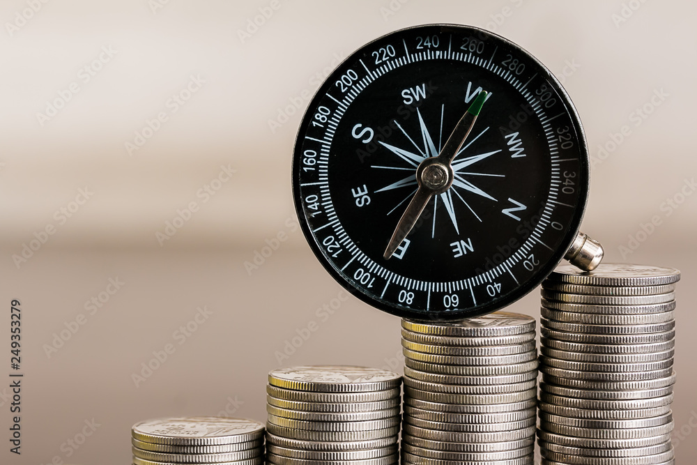 Stack of coins with compass on wood table