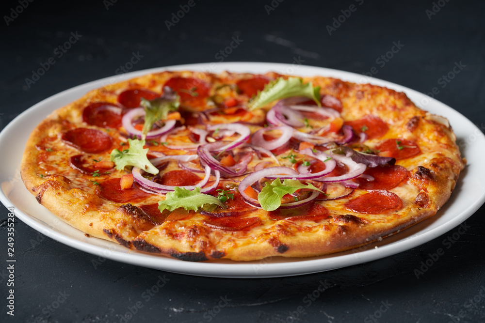 Fresh italian salami hot pizza with green leaves on black organic background Fresh italian salami hot pizza with green leaves on black organic background