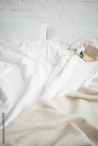 book and glasses on empty cozy white bed