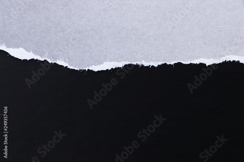 Ragged edge of gray paper on black surface. Empty background.