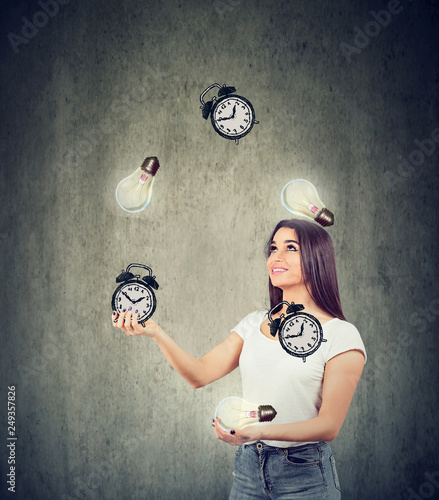 Happy young woman juggling bright lightbulbs and alarm clocks
