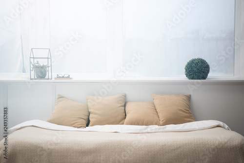 bedroom with brown pillows and white blanket on empty bed  plants and glasses