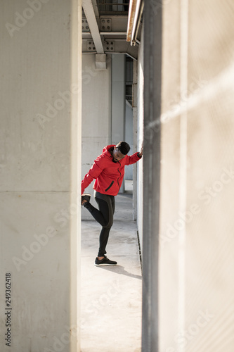 Black athlete stretching quadriceps during running urban workout.