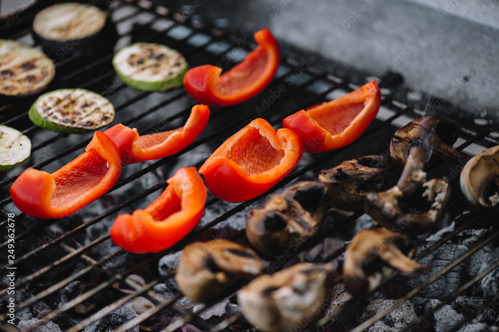 selective focus of red bell pepper, zucchini and mushrooms grilling on barbecue grill grade