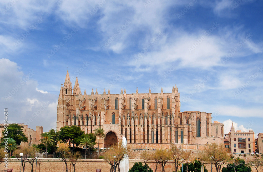 View of the Cathedral Basílica de Santa María de Mallorca during a summer day, against a blue sky covered by white clouds.