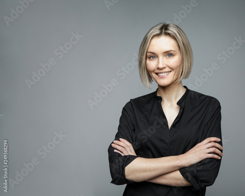 Beautiful middle-aged woman on a gray background in a black blouse smiling.
