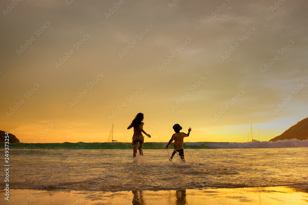 The couple of happy young people on the beach is running with children jumping in the on a background of sunset beach and sea
