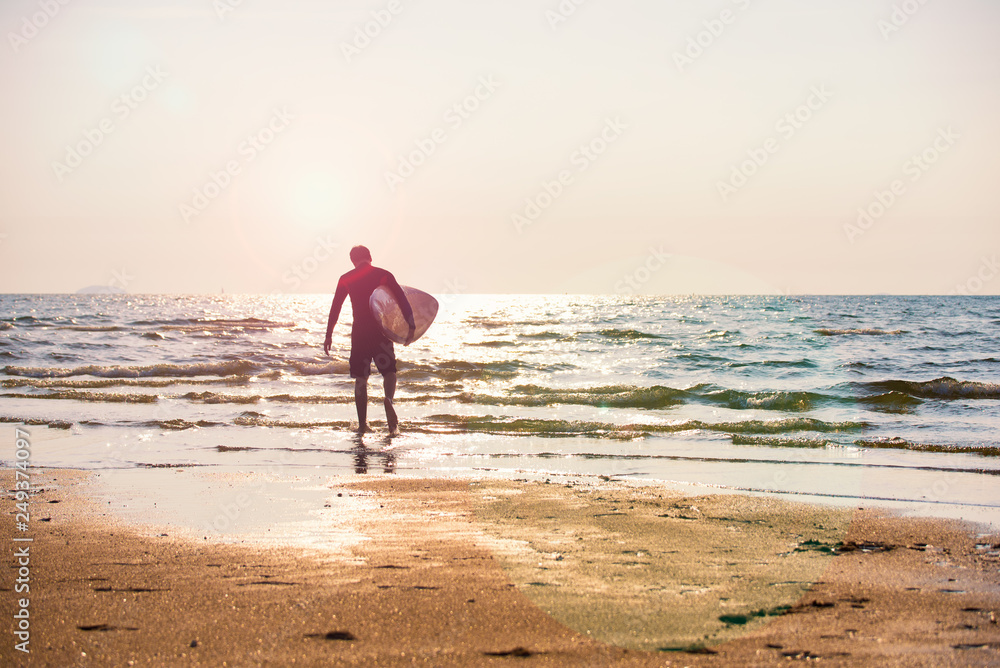 Young man holding surfboard running on the seashore with sunlight and flare., Summer activity of people on the beach concept.
