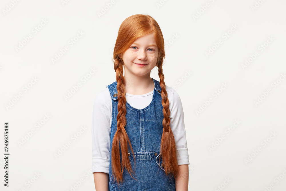 Nice kind girl with red hair woven into two braids, smiling affably dressed in jeans overall dress over a white longsleeve isolated on white background Nice kind girl with red hair woven into two braids, smiling affably dressed in jeans overall dress over a white longsleeve isolated on white background