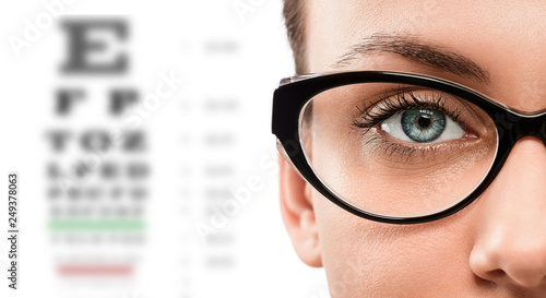 Cloese up of young woman wearing eyeglasses with eyechart in the background photo