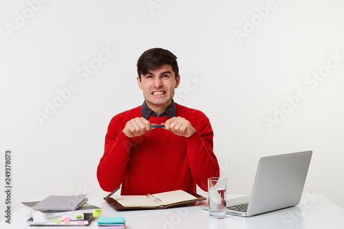 Tableau sur toile Employee is sitting in the office at the table, he is angry, holding a pen in his hands that is ready to break