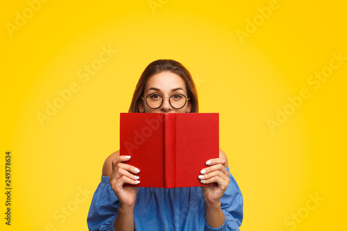 Woman in glasses holding book near face