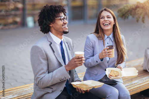 Smiling businessmen with paper cups sitting in front of the office building - lunch break