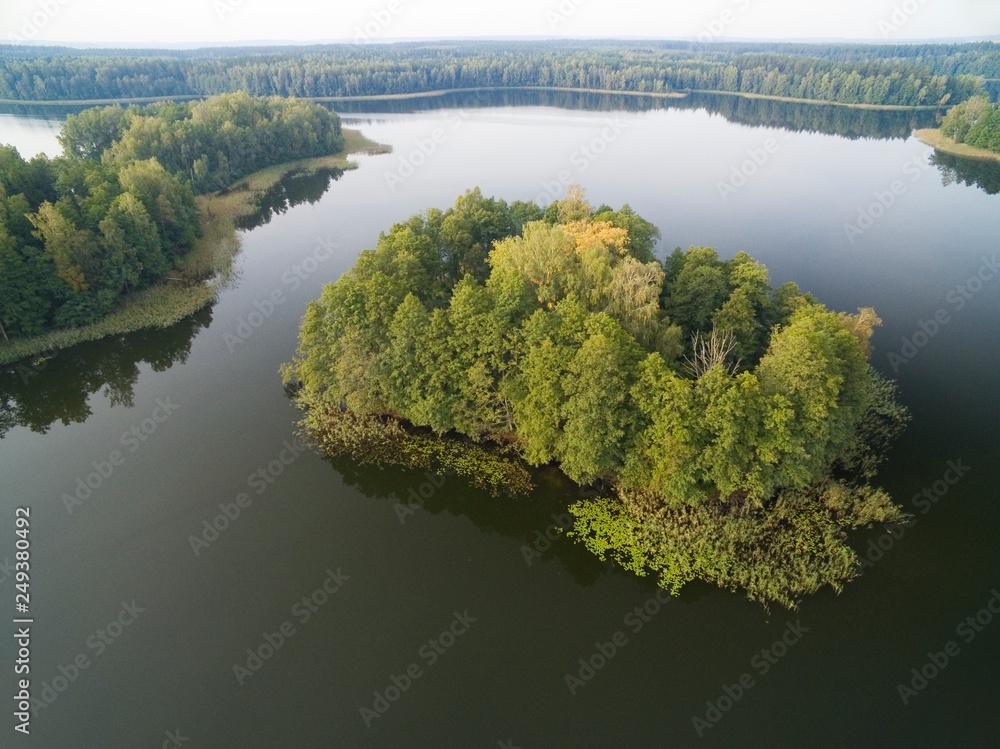 Aerial view of small uninhabited island (Wyspa Pozeracza Serc) on lake with sky reflected in calm water during autumn season, Krzywa Kuta Lake, Mazury, Poland Aerial view of small uninhabited island (Wyspa Pozeracza Serc) on lake with sky reflected in calm water during autumn season, Krzywa Kuta Lake, Mazury, Poland