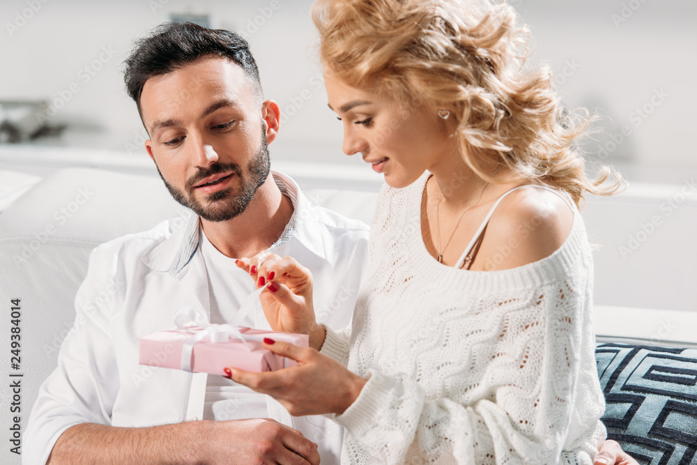 Charming girl sitting on sofa with boyfriend and holding gift Charming girl sitting on sofa with boyfriend and holding gift