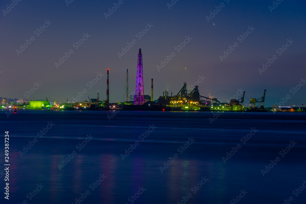 大煙突のある夕方の工場夜景と波間の輝き