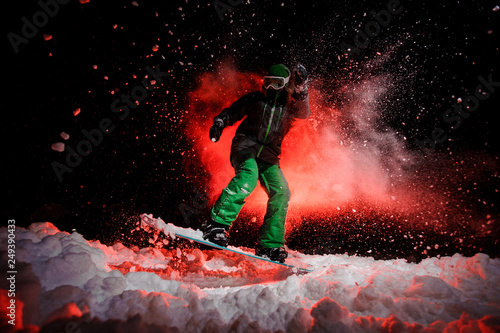 Girl on the snowboard dressed in a green sportswear jumping on the snow