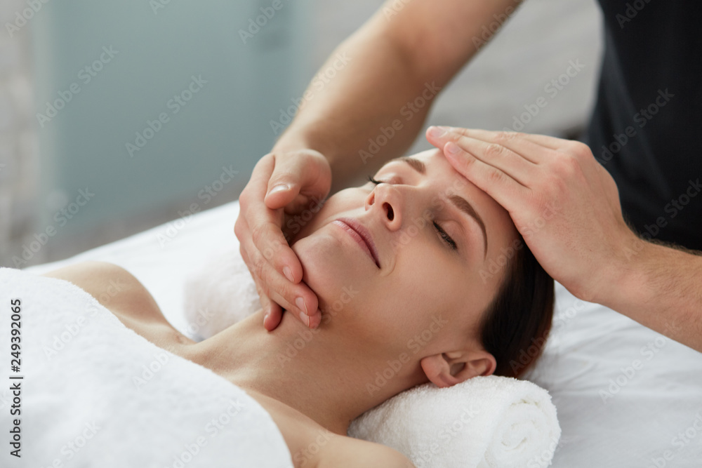 Young beautiful woman enjoying anti-aging facial massage.Male therapist making head massage to female client.Professional masseur.Relaxation,beauty,spa,body and face treatment concept. Young beautiful woman enjoying anti-aging facial massage.Male therapist making head massage to female client.Professional masseur.Relaxation,beauty,spa,body and face treatment concept.