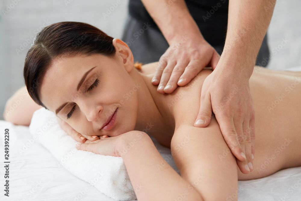 Young beautiful woman enjoying a back massage. Professional massage therapist is treating a female patient in apartment. Relaxation, beauty, body and face treatment concept. Home massage. Young beautiful woman enjoying a back massage. Professional massage therapist is treating a female patient in apartment. Relaxation, beauty, body and face treatment concept. Home massage.