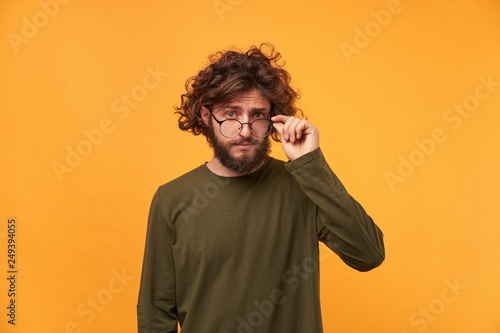 Tthe young professor lowers his glasses with interest and examines something new. Bearded curly-headed man looked something curious and takes off his glasses