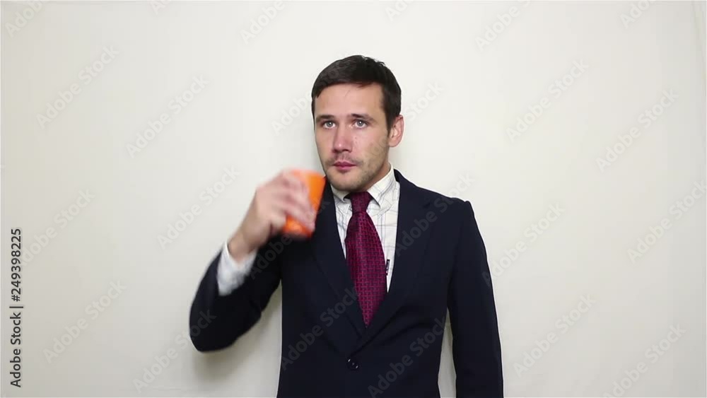 Young handsome businessman is tormented by thirst and he enjoys drinking water from an orange cup. Portrait on white background
