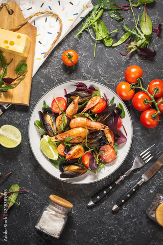 Fresh seafood salad, mussels, shrimp, fresh vegetables and herbs on black stone background
