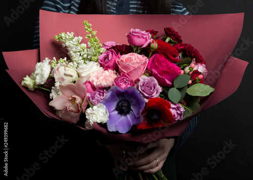 Fototapeta Naklejka Na Ścianę i Meble -  A beautiful bouquet of rare flowers with anemones, ranunculus, carnations, lilac, in the hands of a girl in a striped sweater.