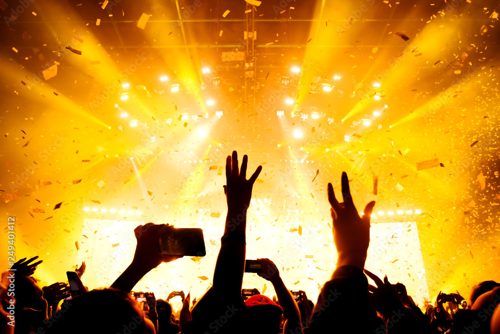 Hands raised up in the crowd of music show in the warm lights of stage. Confetti in the air Hands raised up in the crowd of music show in the warm lights of stage. Confetti in the air