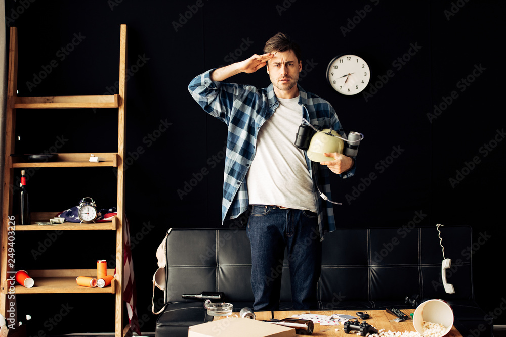 Fototapeta premium handsome man holding beer helmet in hands and standing in messy living room